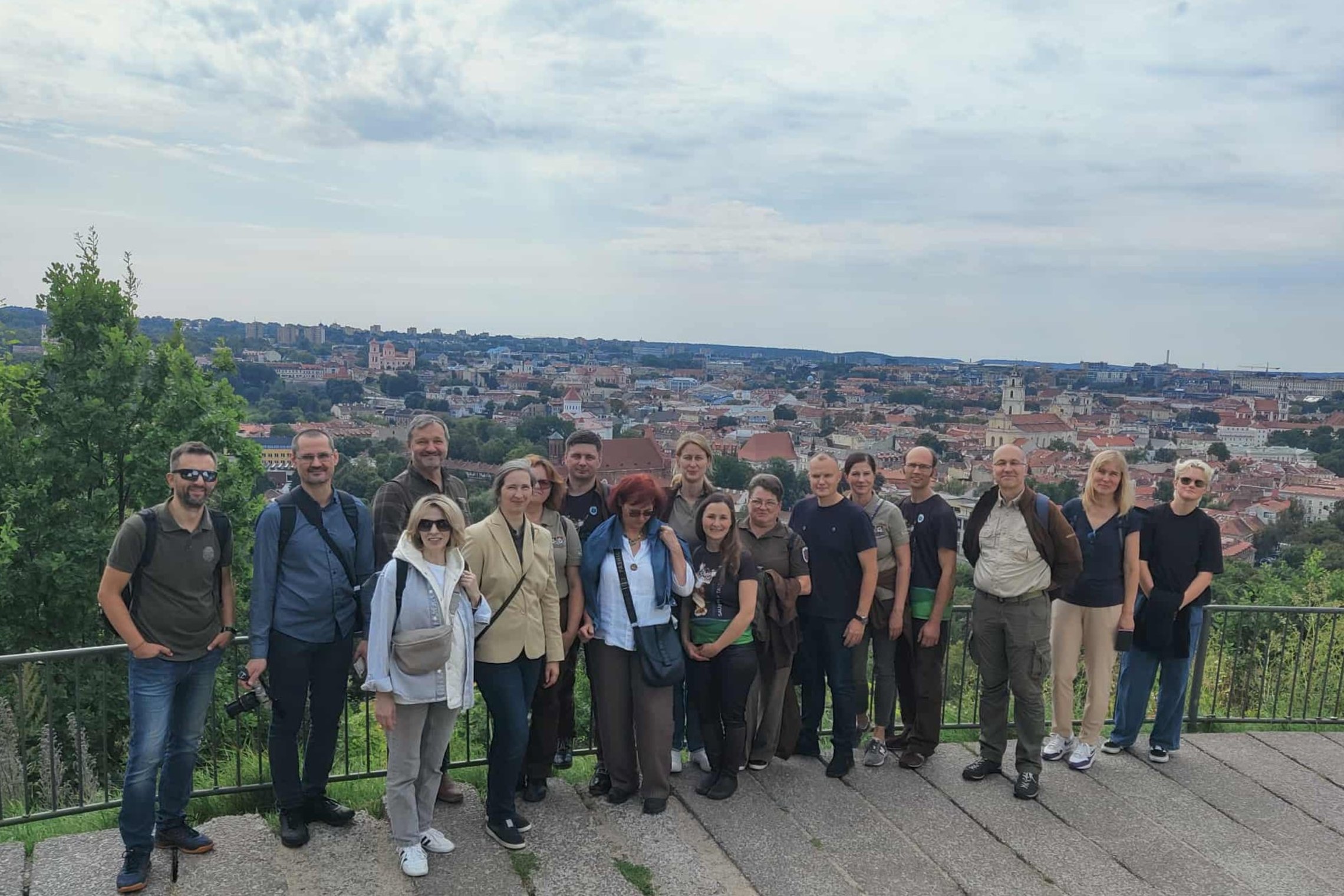 Grupė saugomų teritorijų darbuotojų stovi Vilniaus pilių rezervate ant kalno, o už jų nugarų atsiveria plati Vilniaus senamiesčio panorama su raudonų stogų jūra.