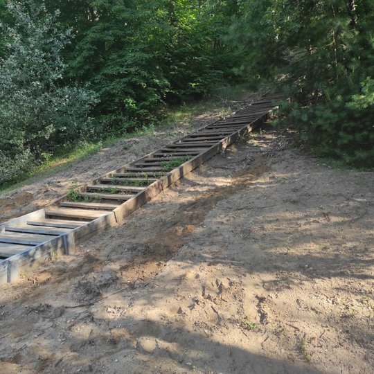 Bekešo mediniai laiptai. Abipus laiptų pilkuoja žemių sąnašų plotai, kuriuose rangosi vandens išgriaušti grioviai. Ypatingai arčiau papėdės - platesni ir gilesni. Dešinėje laiptų besišakojanti mažesnė išgrauža, o kairėje – daug gilesnės ir platesnės dvi i