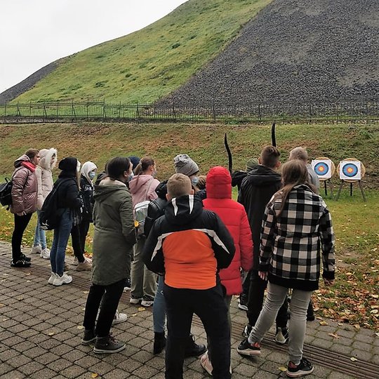 Mokiniai Gedimino kalno papėdėje šaudo iš lanko į taikinius. Nuotraukos centre matosi Gedimino pilies bokštas.