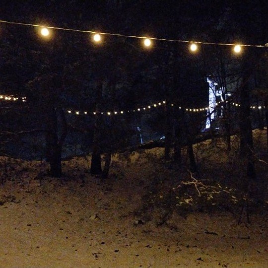 Naktis Trijų Kryžių kalne. Daug sniego. Nuotraukos dešinėje daug pušų. Trijų Kryžių kalno laiptai kyla į viršų. Virš jų kabo kalėdinių girliandų lemputės. Jos gražiai šviečia.
