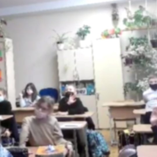 Graži su daug vaikų piešinių ant spintos mokinių klasė/ Vaikai susidomėję klausosi nuotoliniu būdu vedamos edukacijos. Beveik visi su veido medicinėmis kaukėmis. Ant spintų labai daug žalių kambarinių augalų.