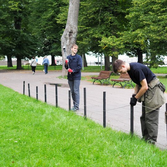 Du vyrai parke tvirtina virvę prie medinių stulpelių palei taką.