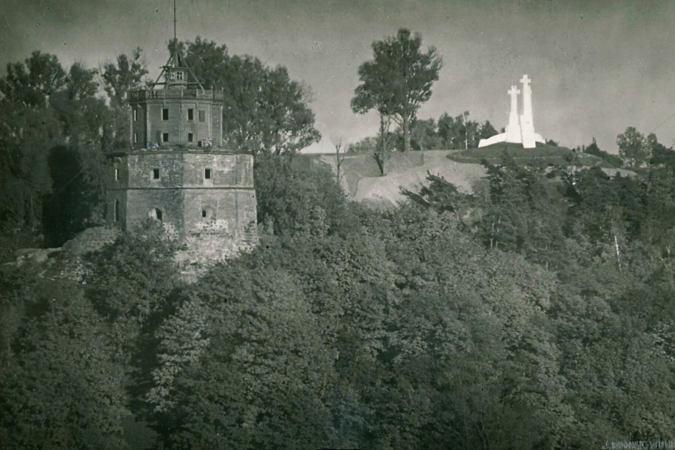 Senoviškoje nuotraukoje Gedimino pilies bokštas yra dviejų aukštų su mediniu antstatu ant viršaus. Dešinėje baltuoja Trijų Kryžių paminklas.