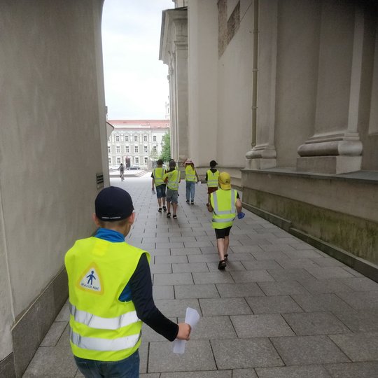 Vaikai apsirengę ryškiomis šviesą atspindinčiomis liemenėmis bėgioja aplinkui katedros aikštę.