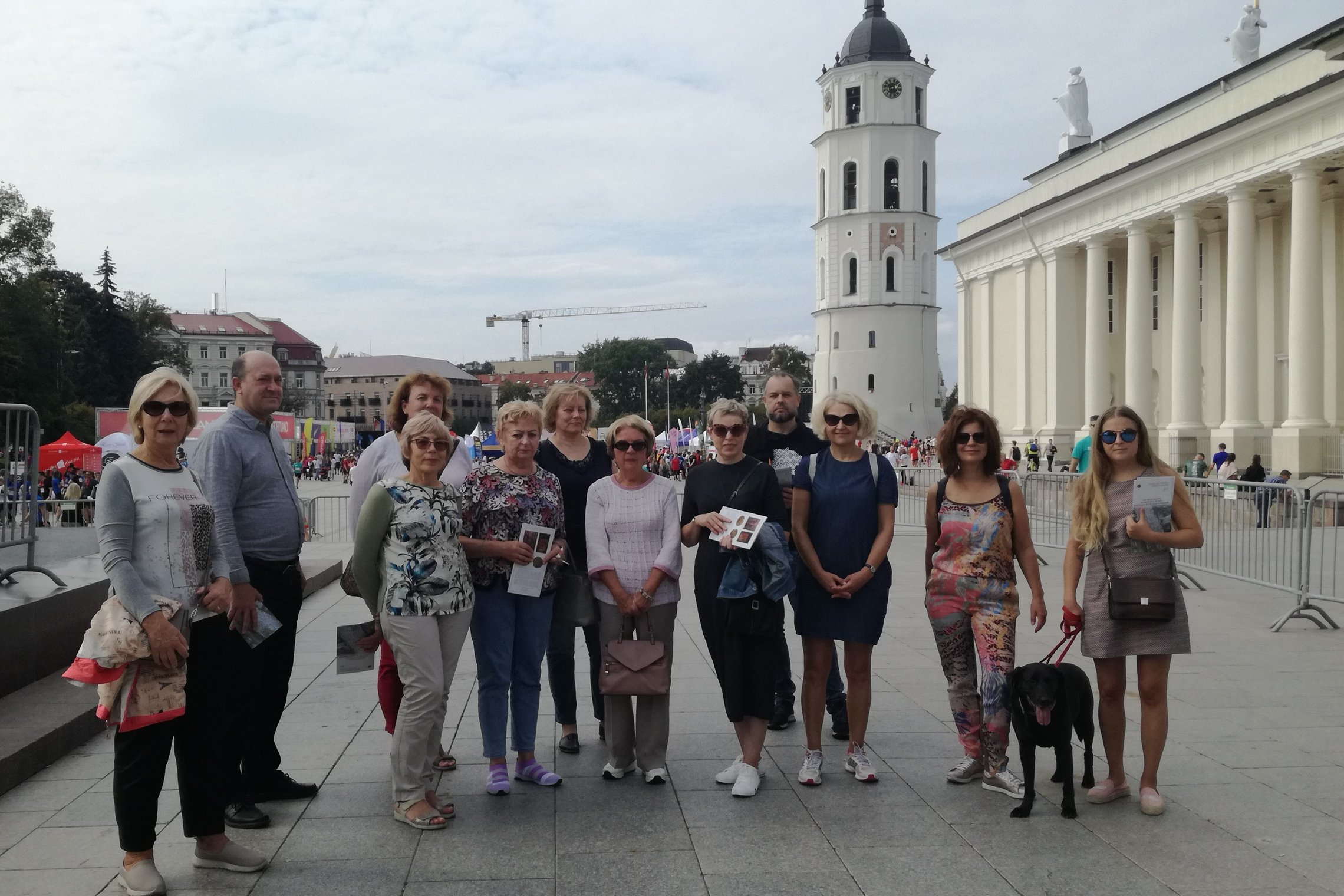 Grupė žmonių pozuoja nuotraukai Katedros aikštėje. Už jų nugaros matosi Katedros varpinė ir Katedra.