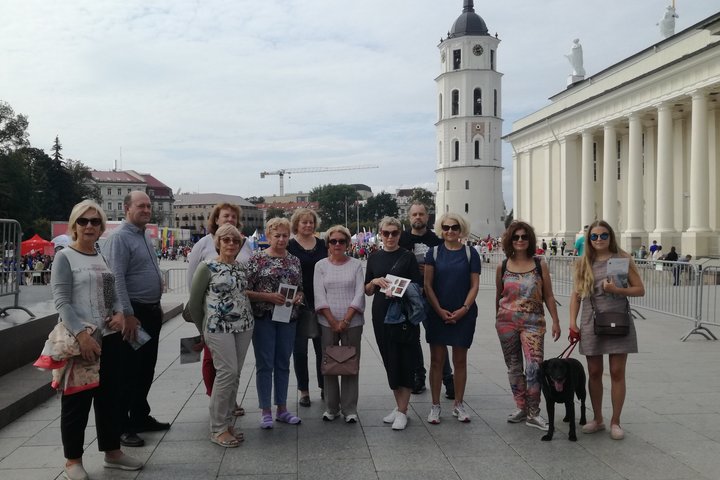 Grupė žmonių pozuoja nuotraukai Katedros aikštėje. Už jų nugaros matosi Katedros varpinė ir Katedra.