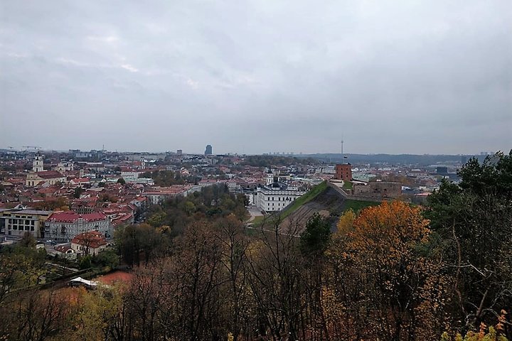 Rudeninis vaizdas į Vilniaus pilis nuo Trijų Kryžių kalno. Matosi Valdovų rūmai, Gedimino pilis ir visas miestas. Pilki debesys danguje, lietinga diena.