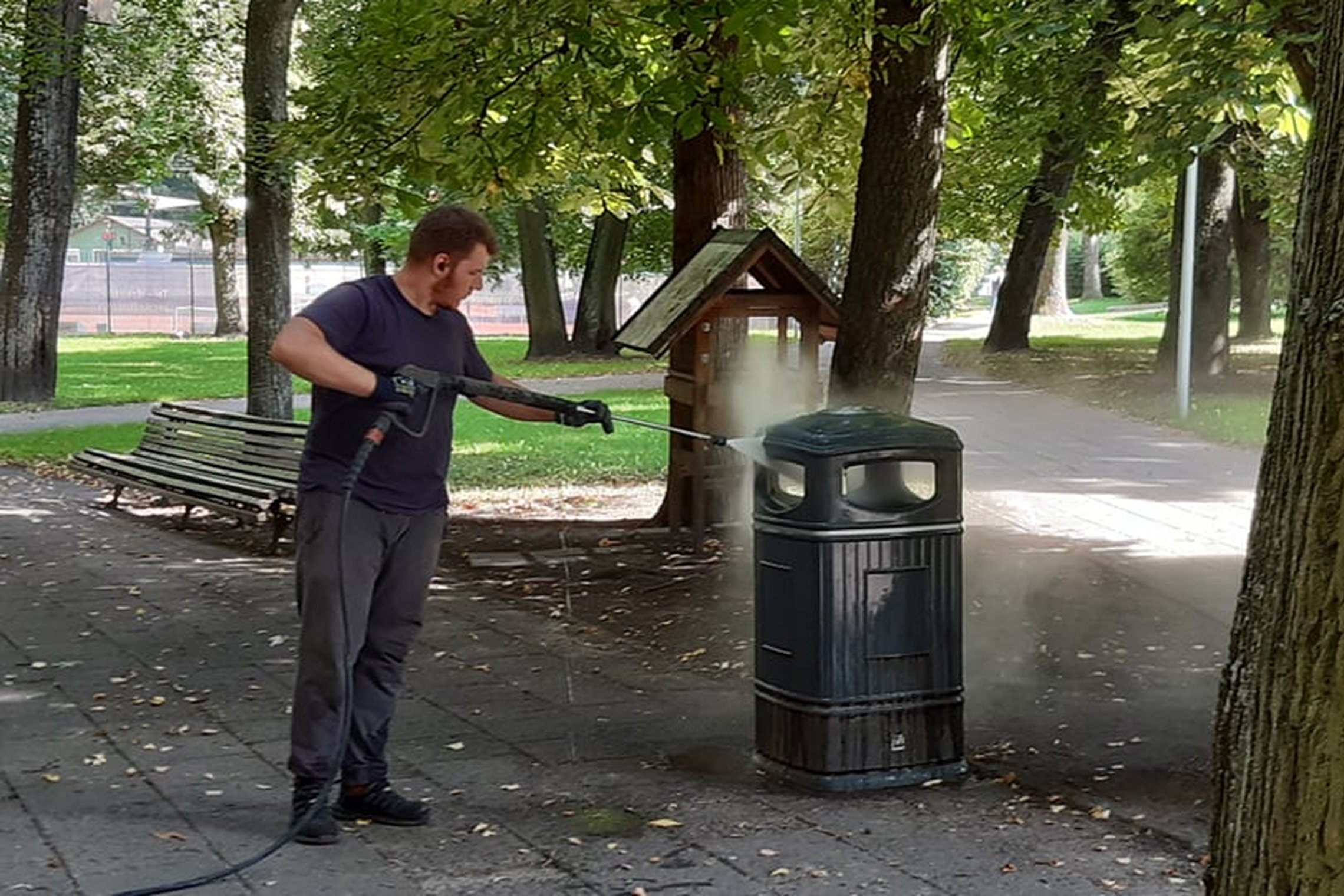 Parkas. Ties dviejų, grįstų šaligatvio plytelėmis parko takų susikirtimu stovi nemaža šiukšliadėžė. Ji keturkampė, su nukeliamu viršumi, tamsiai žalia. Toliau šiuos takus kerta dar vienas takas. Tarp takų gausu parko medžių su lygiais neplonais kamienais.