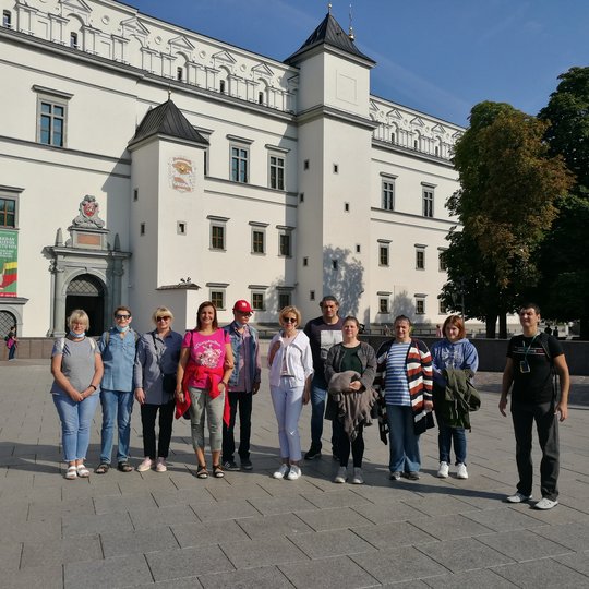 Grupė ekskursijos dalyvių stovi Valdovų rūmų fone.
