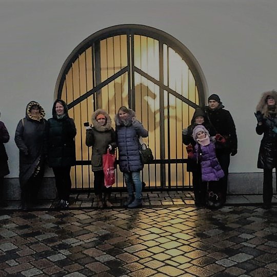 Grupelė žmonių stovi prie pastato, kuris turi arkinį langą. Lango gilumoje šviečia Vyčio kontūrai - karys iškėlęs rankoje kalaviją, sėdi ant žirgo. Tarp žmonių yra vienas vaikas. Visi stovi ant mozaikinio šaligatvio.