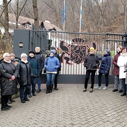 Ekskursijos dalyviai pozuoja šalia geležinių vartų su didžiuliu herbu. Tai Nyderlandų ambasadoriaus rezidencija. Herbas susideda iš dviejų liūtų, kurie laiko skydą. Skyde pavaizduotas dar vienas liūtas. Virš skydo – karaliaus karūna.
