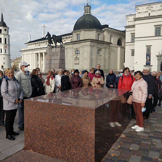 Ekskursijos dalyviai prie buvusių Pilies vartų. Dabar juos žymi raudono granito blokai. Už žmonių nugarų yra Vilniaus katedra ir Valdovų rūmai.