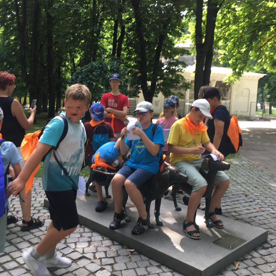 Vaikai žaidžia prie lietuvių skalikų skulptūrų Pilių parke. Jie po kelis sėdi ant skalikų nugarų.