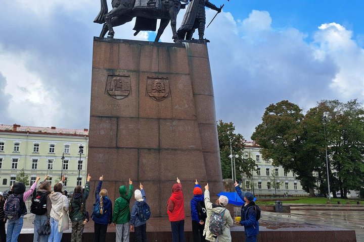 Grupė penktokų iš Sietuvos gimnazijos stovi prie Gedimino paminklo Vilniuje ir rodo rankomis į viršų, link skulptūros.