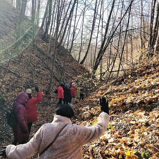 Ekskursijos dalyviai eina vorele takeliu Didžiojoje griovoje. Aplink kalnai ir nukritę medžių lapai. Saulėta rudens diena.