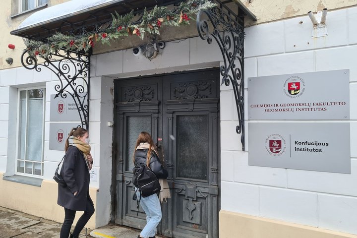 Vilniaus universiteto Medicinos fakulteto ir Geomokslų instituto centrinis įėjimas su gražius, metalu dekoruotu stogeliu. Ant stogelio pritvirtinta kalėdinė dekoracija - eglių girlianda su papuošimais. Prie durų yra dvi merginos, kurios eina į pastatą.