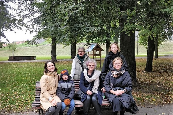 Nedidelė grupelė žmonių sėdi Pilių parke ant suolo ir pozuoja nuotraukai. Tai ekskursijos alyviai.