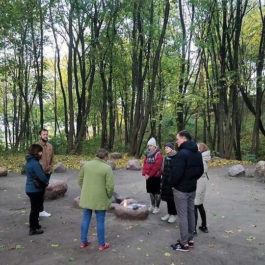 Nedidelė grupelė žmonių stovi aplink amžinąją ugnį, kuirią kūrena Agnijos klubo nariai.