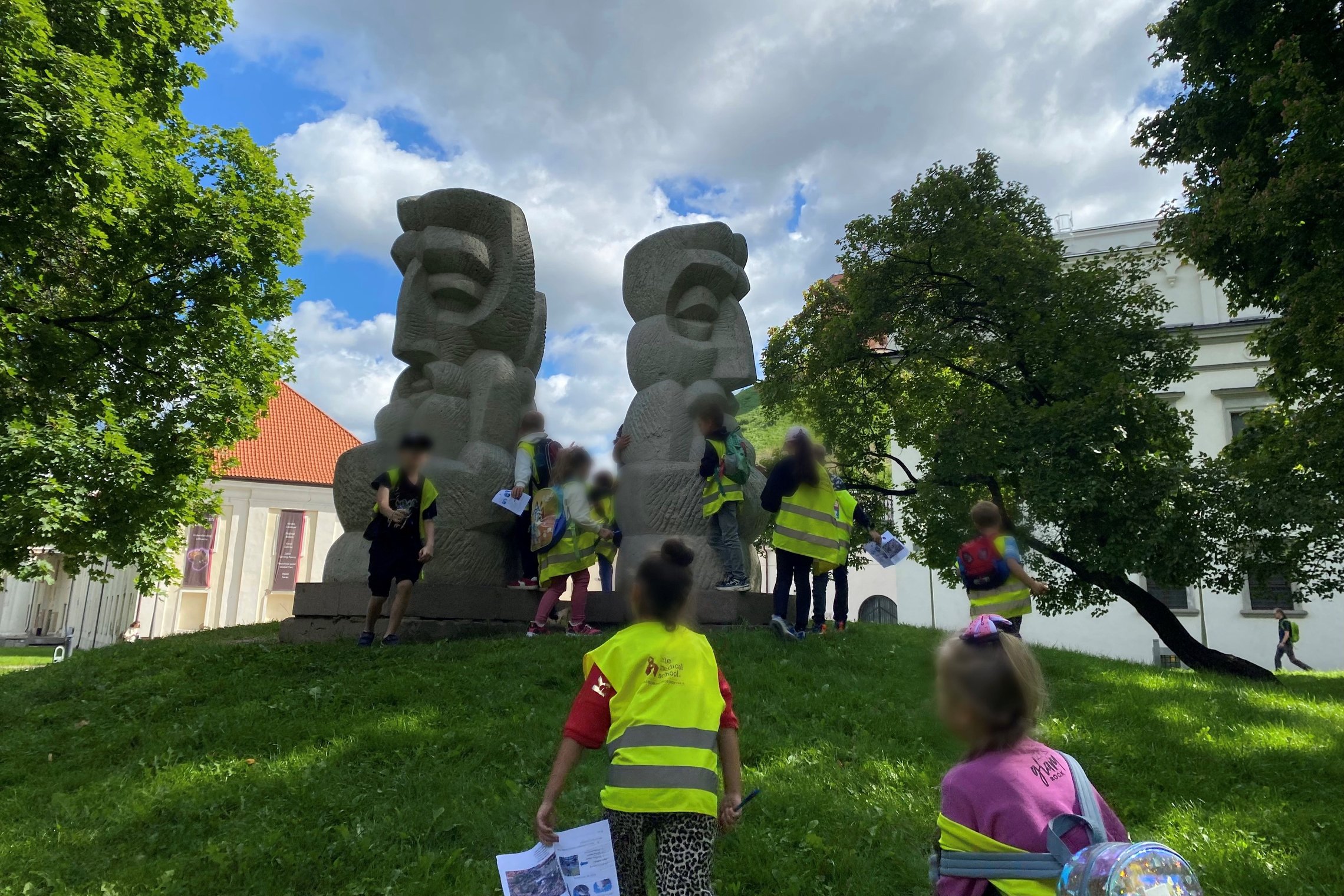 Vaikai su saugos liemenėmis tyrinėja skulptūras Vilniaus Katedros aikštės prieigose edukacijos metu