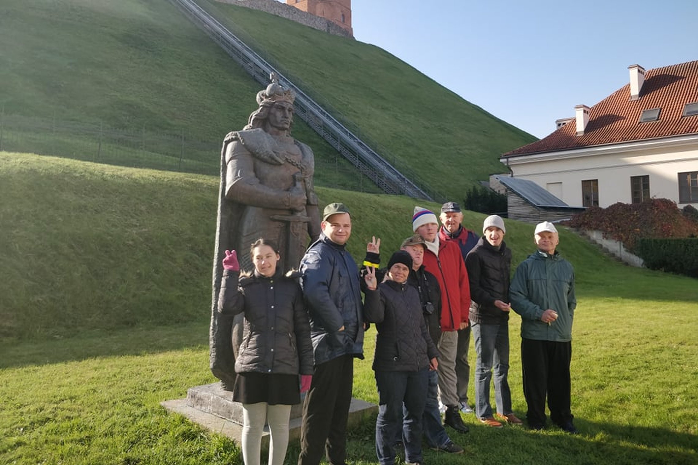 Nedidelė ekskursijos grupė išsirikiavusi prie Vytauto paminklo Gedimino kalno papėdėje. Į kalną kyla funikulieriaus bėgiai. Dešinėje ant kalno matosi Gedimino pilies bokštas. Kalno papėdėje dar matosi pastatas - tai muziejus.