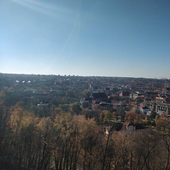 Nuostabi ir šilta rudens diena ir nuotraukoje daug vaiskaus dangaus. Nei vieno debesėlio. Vaizdas nuo Trijų kryžių kalno. Nuotraukos pirmame plane - daug medžių. Jie jau numetę lapus.
