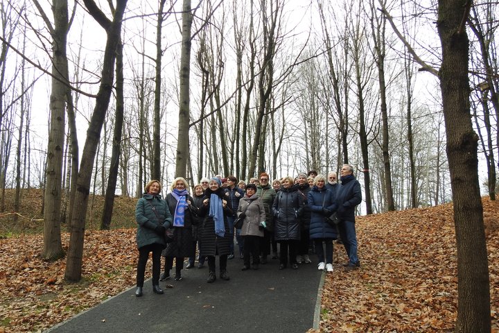 Didelė ekskursijos grupė stovi dabartiniame Kalnų parke ant naujai išasfaltuoto tako. Visi medžių lapai yra nukritę ant žemės, tad tai vėlyvas ruduo, tačiau nėra šalta.