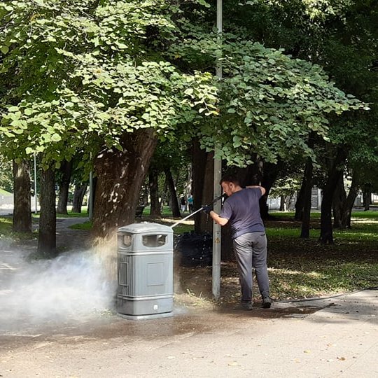 Ties dviejų, grįstų šaligatvio plytelėmis parko takų susikirtimu stovi nemaža šiukšliadėžė. Ji keturkampė, su nukeliamu viršumi, tamsiai žalia. Jaunas vyriškis, apsirengęs tamsiai pilkais, trumpom rankovėm marškinėliais, tokios pat spalvos kelnėm, storapa