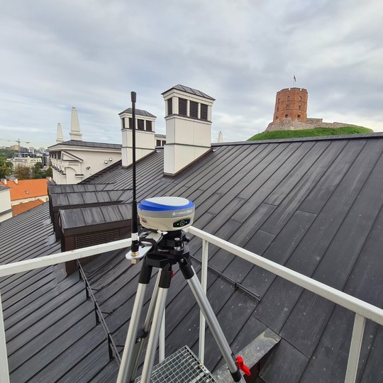 Ant Valdovų rūmų stogo pastatyta geodezinio GNSS imtuvo bazinė stotis. Virš stogo matosi tolumoje Gedimino pilies bokštas.