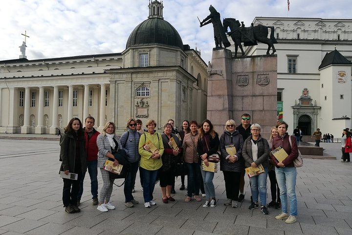 Nemaža grupė ekskursijos dalyvių pozuoja nuotraukoje prie Gedimino paminklo. Jų fone Katedra ir Valdovų rūmai.
