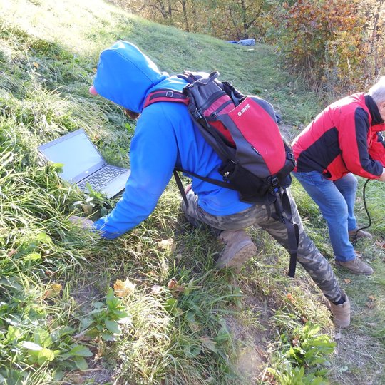 Lietuvos geologijos tarnyba tiria Trijų Kryžių kalną. Keli žmonės kalno šlaite daro tyrimus.