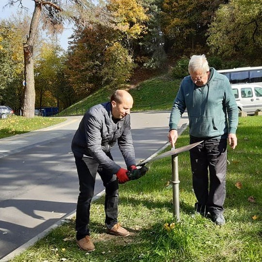Saulėta rudens diena Kalnų parke. Pėsčiųjų takas driekiasi tolyn ir dingsta pasiekęs nuokalnę. Abipus tako augantys medžiai ir krū ilgus šešėlius skersai tako apiberto geltonais ir parudusiais lapais. Nuotraukoje jų kamienai meta ilgus šešėlius skersai ta