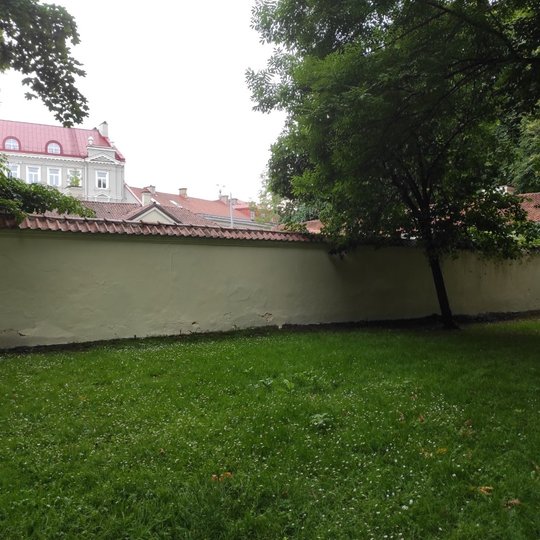Kirdėjų rūmų tvora naujai išdažyta, jokių užrašų. Šalia tvoros auga parko medžiai.