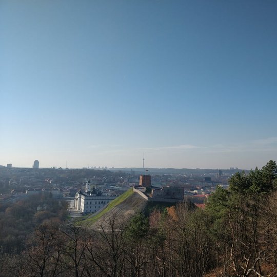 Nuostabi ir šilta rudens diena ir nuotraukoje daug vaiskaus dangaus. Nei vieno debesėlio. Vaizdas nuo Trijų kryžių kalno. Matosi Gedimino pilis, Valdovų rūmai ir visas miestas. Nuotraukos pirmame plane - daug medžių. Jie jau numetę lapus. 