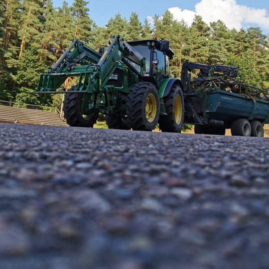 Didžiulis traktorius su priekaba, kurioje yra nupjauta mediena, kurią ruošiasi išvežti. Traktorius stovi Dainų slėnio slėnio estradoje.