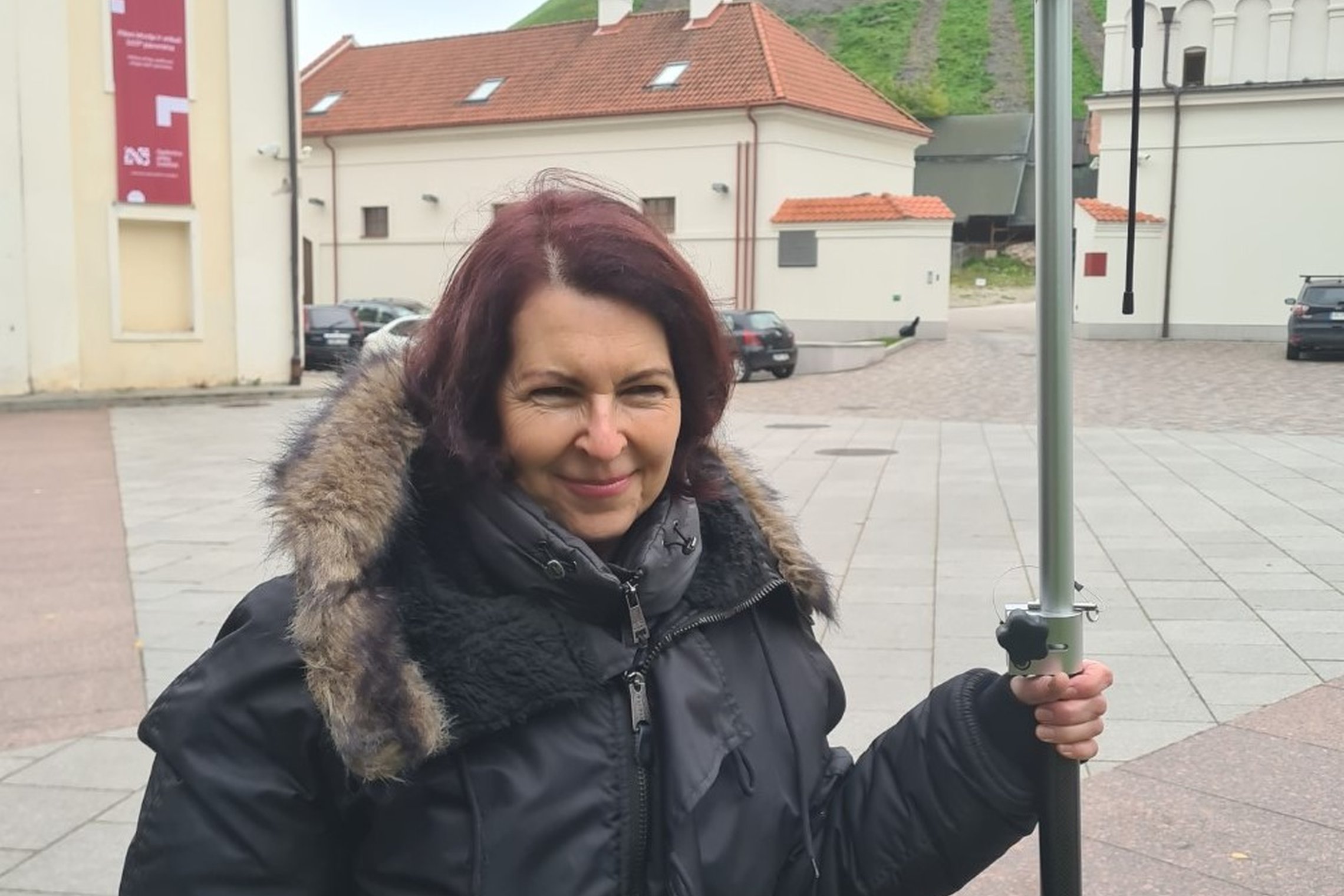 Stovi moteris, kuri laiko geodezinį GNSS imtuvą. Tiksinamas Vilniaus pilių teritorijos topografinis planas. Moteris stovi netoli Valdovų rūmų ir Gedimino pilies kalno.
