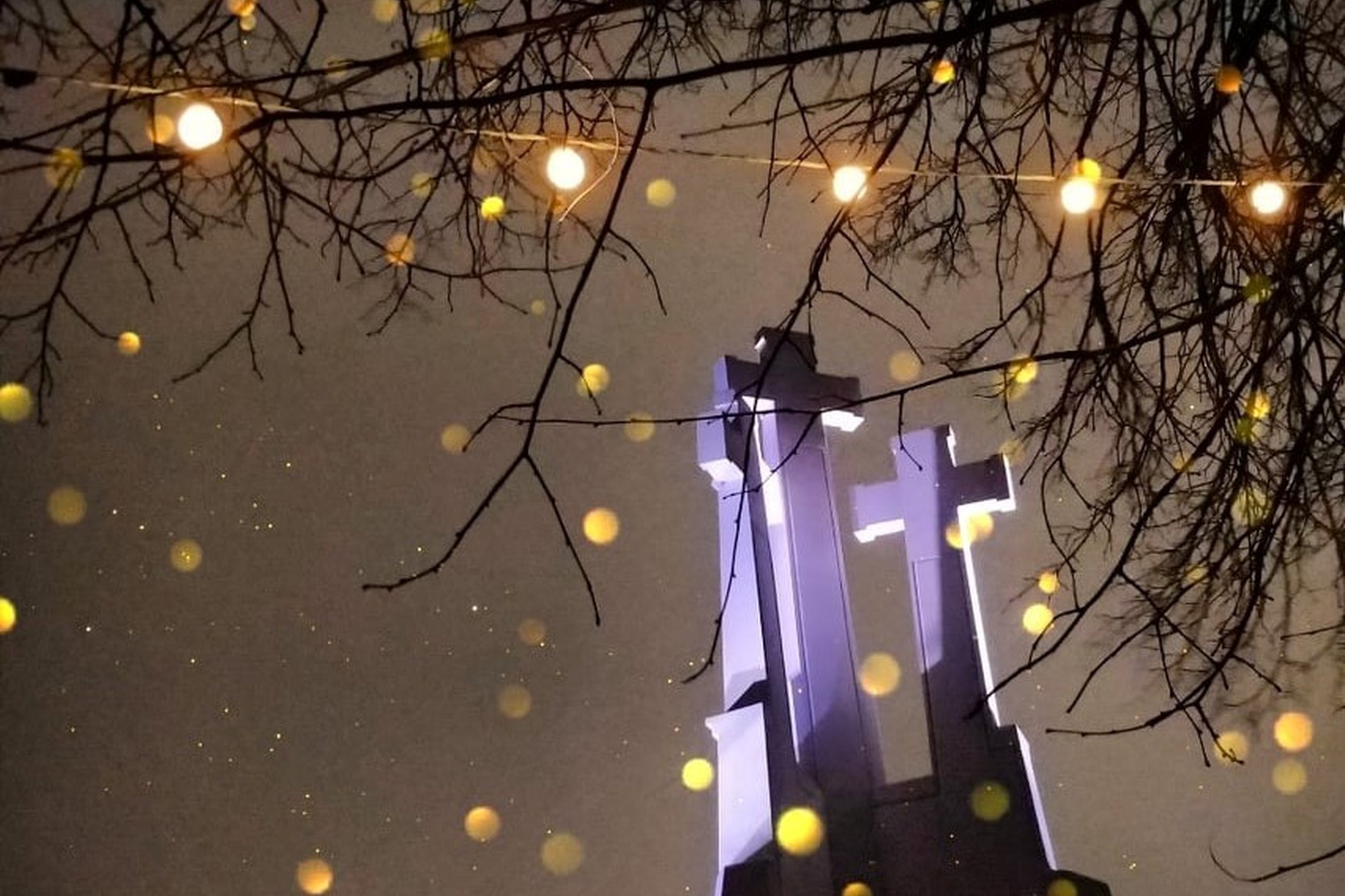 Nakties fone apšviesas Trijų Kryžių paminklas. Ant medžių šakų kabo kalėdinės girliandų lamputės. Jos taip pat šviečia.
