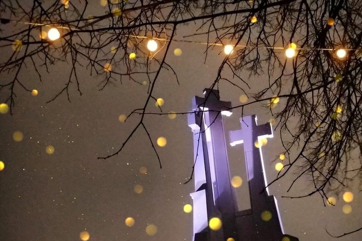 Nakties fone apšviesas Trijų Kryžių paminklas. Ant medžių šakų kabo kalėdinės girliandų lamputės. Jos taip pat šviečia.