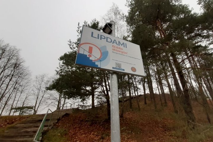 Kelių pušų fone yra iškelta ant ilgo koto lentelė - LIPDAMI BŪKITE ATSARGŪS. Tai perspėjimas žmonėms, nes Trijų Kryžių kalno laiptai laukia tvarkymo darbų.