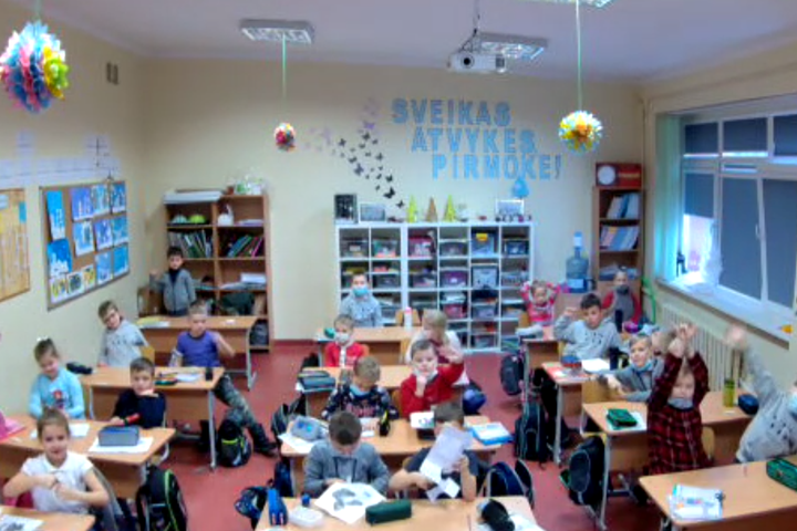 Nuotraukoje pirmokėlių klasė. Fotografuota iš klasės priekio ir iš aukščiau, todėl gerai matyti visa klasė ir visa kas joje yra. Trys eilės po keturis suolus. Sienos gelsvos, lubos baltos. Dešinėje du didžiuliai langai, tarpulangyje siena išpiešta gėlėmis
