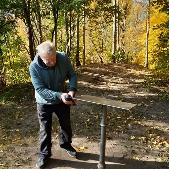 Saulėta rudens diena Kalnų parke. Pėsčiųjų takas driekiasi tolyn ir dingsta pasiekęs nuokalnę. Abipus tako augantys medžiai ir krū ilgus šešėlius skersai tako apiberto geltonais ir parudusiais lapais. Nuotraukoje jų kamienai meta ilgus šešėlius skersai ta