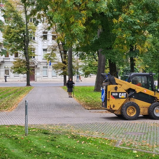 Parko alėjose važiuoja nedidelis butkatas. Nuotraukos centre stovi moteris, kuri tikslina parko topografinį planą.