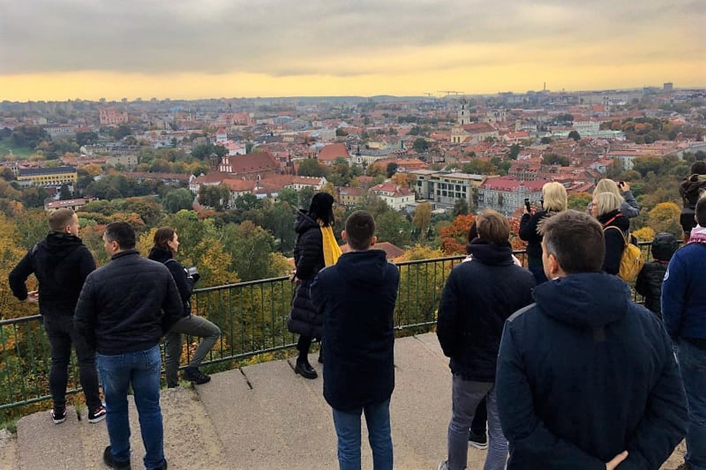  Stovi grupė žmonių ant Trijų Kryžių kalno. Jie žiūri į miesto vaizdą, kuris nuo šio kalno atsiveria labai plačiai. Priekyje stovi ekskursijos gidė.