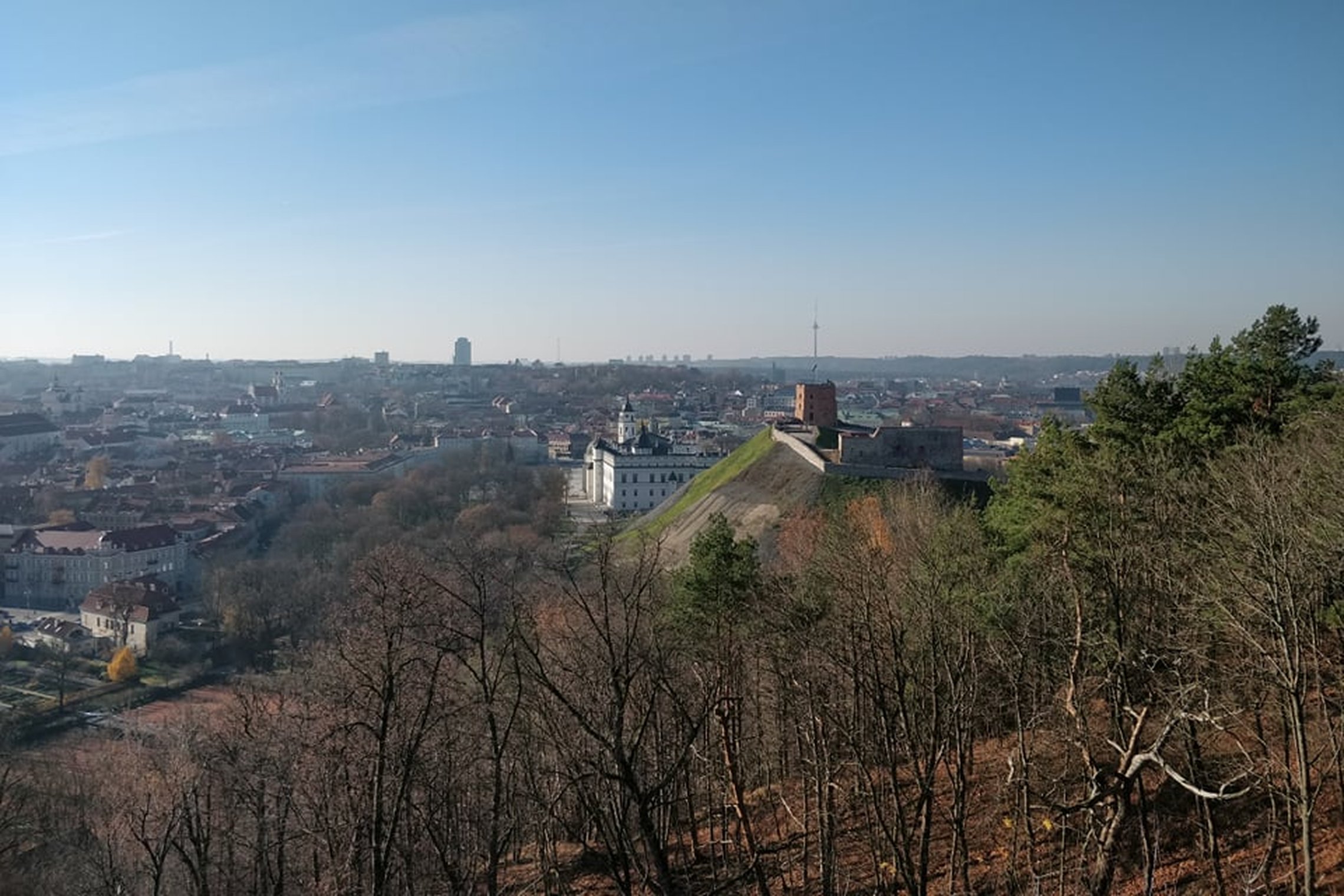 Nuostabi ir šilta rudens diena ir nuotraukoje daug vaiskaus dangaus. Nei vieno debesėlio. Vaizdas nuo Trijų kryžių kalno. Matosi Gedimino pilis, Valdovų rūmai ir visas miestas. Nuotraukos pirmame plane - daug medžių. Jie jau numetę lapus. 