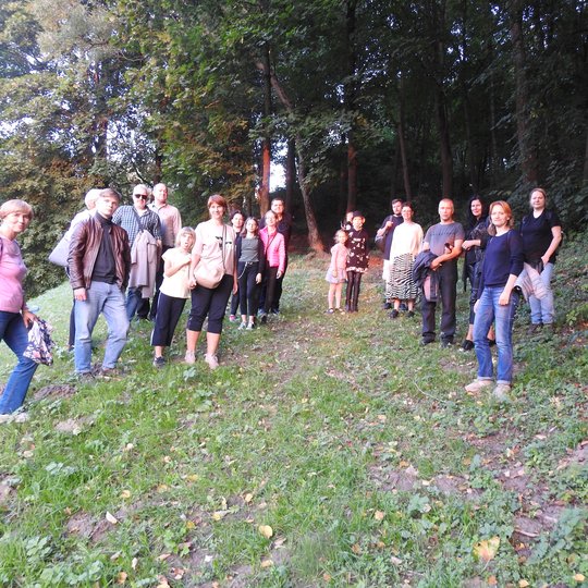 Ekskursijos grupė pozuoja ant žolės, pakeliui einant į medžių tankmę.