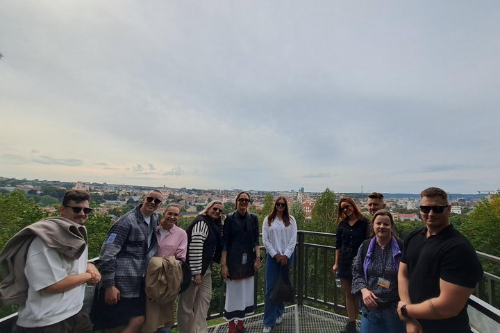 Nuotraukoje grupė žmonių šypsosi į kamerą. Jie stovi Altanos bokštelio terasoje. Fone Vilniaus panorama.
