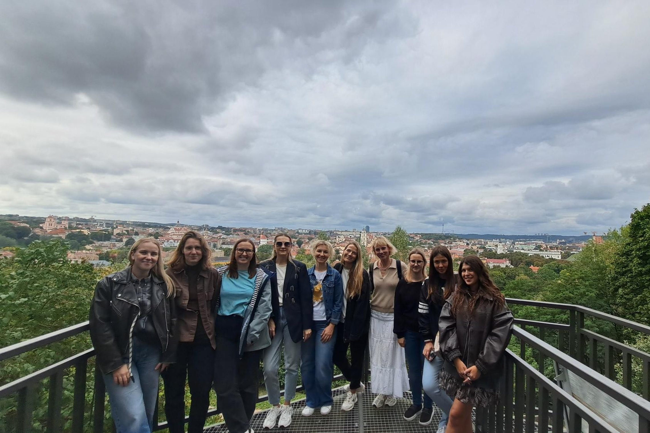 Nuotraukoje žmonių grupė pozuoja Altanos bokštelio terasoje. Už jų nugarų atsiveria viena gražiausių panoramų Vilniuje.