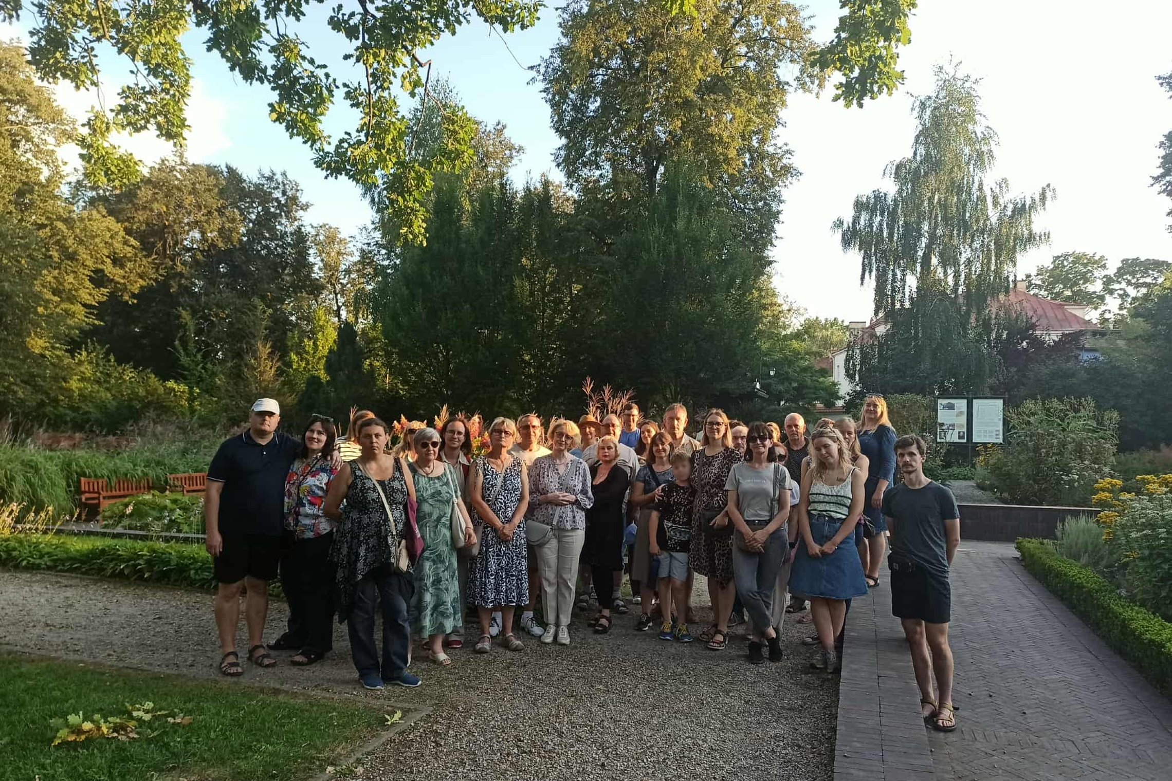 Nuotraukoje didelė žmonių grupė stovi ir pozuoja  parke, aplink matosi medžiai, gėlynai.