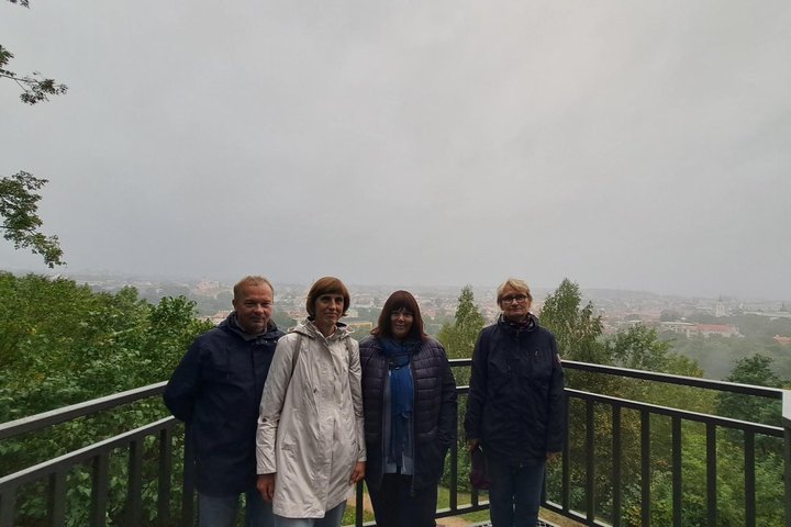 Nuotraukoje žmonės Altanos bokštelio terasoje. Fone apsiniaukęs dangus ir nuostabi Vilniaus panorama.