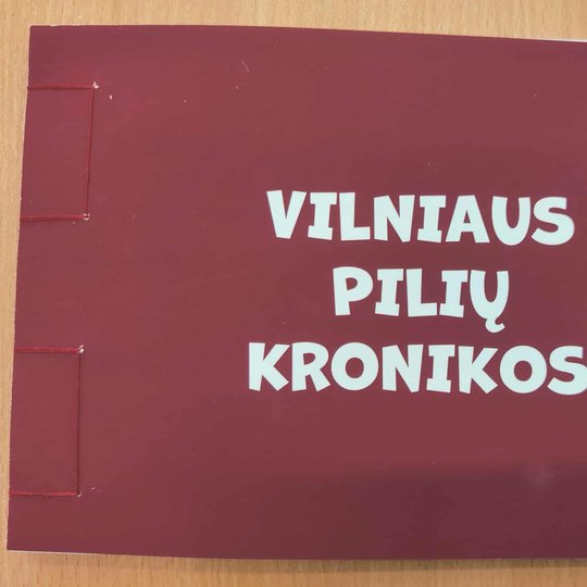 Knygos viršelis: tamsiai raudonos spalvos rankų darbo leidinys su siūtu nugarėlės kraštu, centre baltomis raidėmis užrašytas pavadinimas „Vilniaus pilių kronikos“.