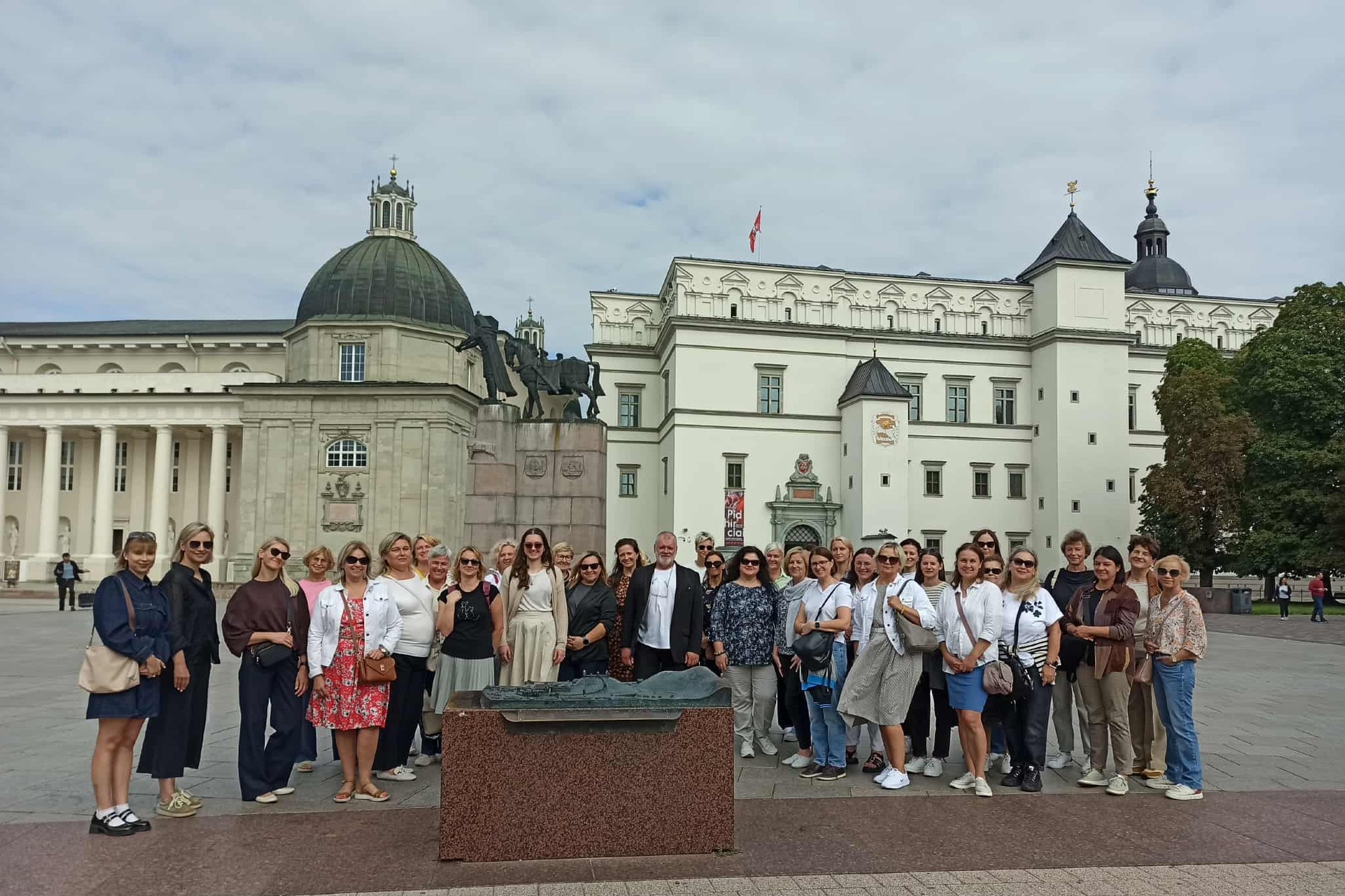 Nuotraukoje didelė žmonių grupė stovi prie pilių maketo. Jiems už nugaros paminklas valdovui Gediminui.